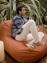 A person seated on a ginger-colored outdoor lounge chair with a tablet in their lap, surrounded by greenery in the background.