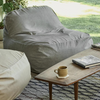 A gray outdoor lounge chair placed on a lawn, next to a wooden side table with a cup and a book on it.