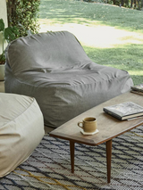 A gray outdoor lounge chair placed on a lawn, next to a wooden side table with a cup and a book on it.