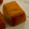 A tangerine-colored velvet ottoman in front of a bed in a stylishly furnished room.