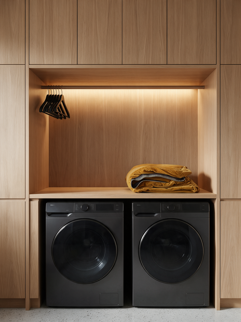 Folded golden furniture slipcover above a black washer and dryer in a wood-paneled laundry area